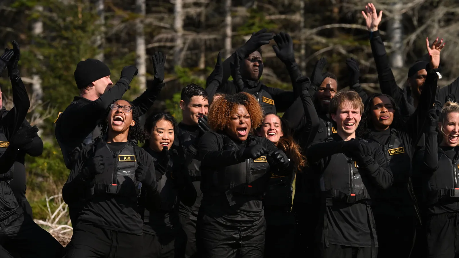 Players in black mission gear celebrate in a forest clearing