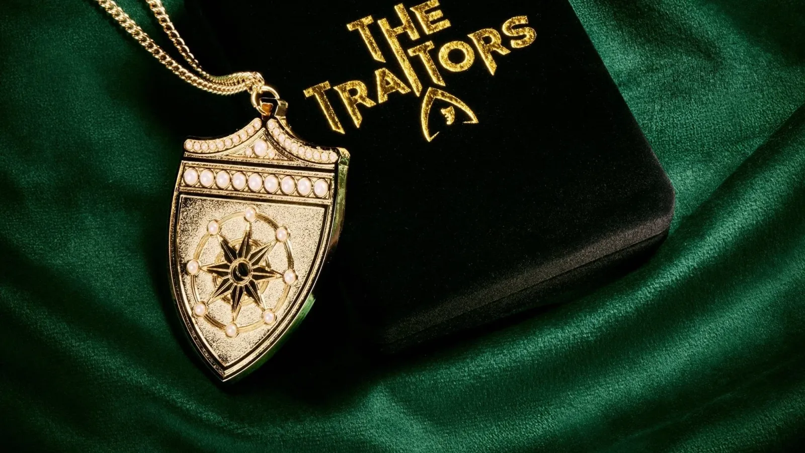 A gold Traitors shield pendant on green velvet